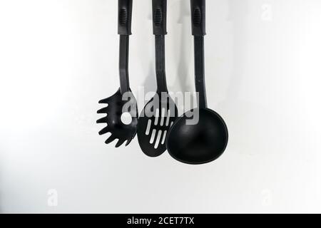 Set of black plastic kitchen utensils hanging on the white wall Stock Photo