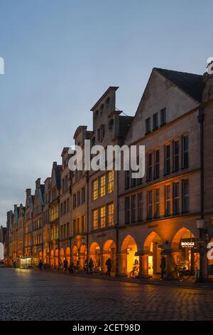 Muenster, Prinzipalmarkt with its old gabled houses at dusk, blue hour, people strolling over world famous shopping street, ancient cobblestone road, Stock Photo