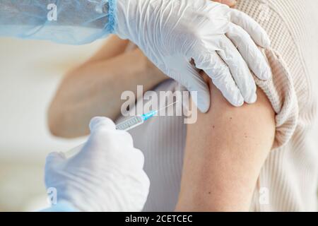 Close-up shot of unrecognizable doctor wearing latex gloves giving Covid-19 vaccine injection into womans shoulder Stock Photo