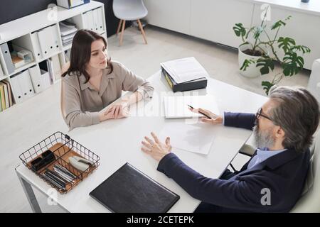 Horizontal high angle view shot of attractive young woman sitting in front of mature man at office desk having job interview Stock Photo