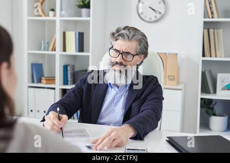 Over-the-shoulder shot of serious mature man wearing eyeglasses working as HR manager interviewing unrecognizable woman Stock Photo