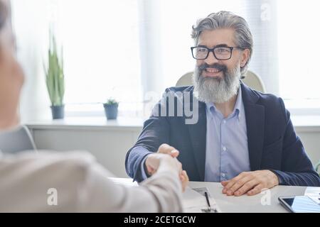 Over-the-shoulder shot of unrecognizable young woman shaking hands with cheerful HR manager after successful job interview Stock Photo
