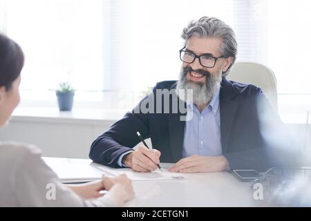 Portrait of cheerful mature HR manager sitting at office desk in front of female applicant interviewing her Stock Photo