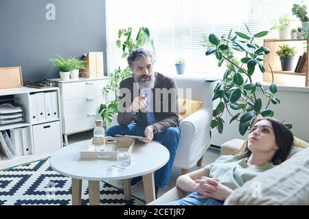 Professional psychologist working with sad young woman on therapy session in his office Stock Photo