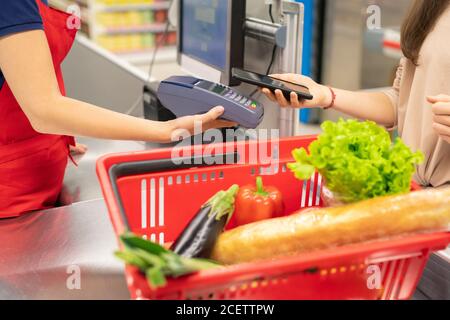 Unrecognizable young woman using NFC application on smartphone to pay for goods in modern store Stock Photo