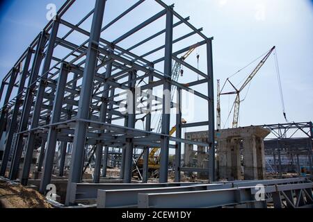 Girder cranes and grey metal grating constructions and concrete support on the blue sky. Construction of new factory buildings in progress. Stock Photo