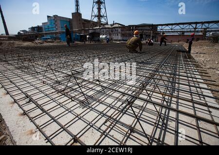 Old phosphate fertilizer plant in modernization. Construction of new industrial buildings. Workers assembling steel reinforcement of building basement Stock Photo