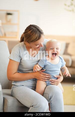 Vertical shot of loving mother sitting in armchair and having fun with her little toddler son on lap