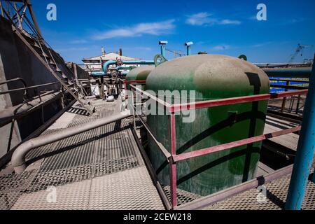 Some green metal tanks and valves and other equipment on mesh (grid) floor. Abstract view of chemical plant. Blue sky background. Stock Photo