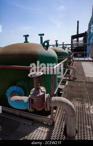 Some rusted metal tanks and valves and mesh floor on blue sky. Abstract view on chemical plant. Stock Photo