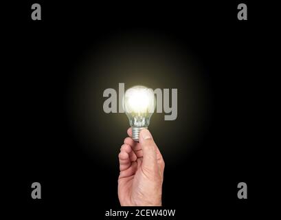 hand holding glowing light bulb against black background, having an idea concept Stock Photo