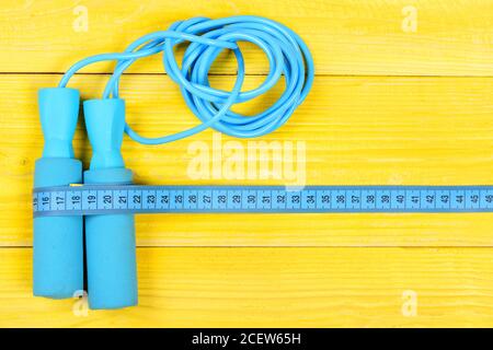 Centimeter tied around sports equipment in cyan blue on wooden vintage  background. Tools for healthy lifestyle. Workout and weight loss concept.  Bottle, apple, measuring tape and jump rope, top view Stock Photo 