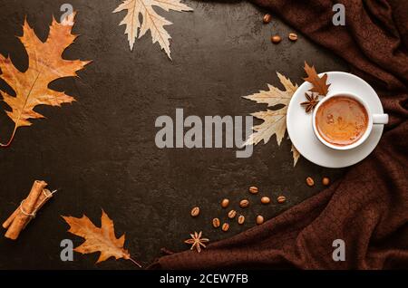 Autumn flat lay. Cup of coffee, brown pashmina scarf, autumn leaves, cinnamon sticks and coffee beans on black background. Copy space. Top view Stock Photo