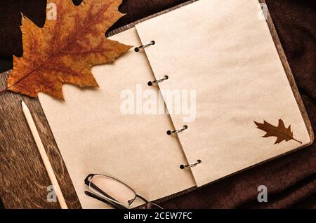 Autumn composition. Notepad with blank sheets, glasses, dry oak leaves on a brown pashmina scarf. Autumn mood. Flat lay. Copy space Stock Photo