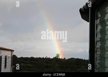 End of a rainbow into the countryside in a dark sky in Pwllheli, North Wales Stock Photo