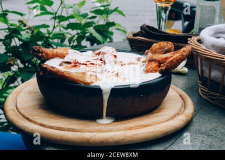 Hot Fried Chicken tobacco with golden brown crust in frying pan on wooden background with herbs and spicy white sauce Stock Photo