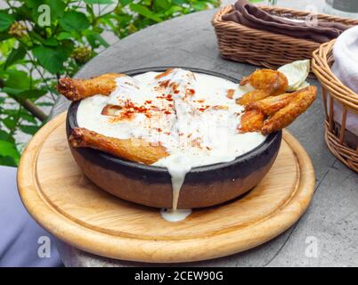 Hot Fried Chicken tobacco with golden brown crust in frying pan on wooden background with herbs and spicy white sauce Stock Photo