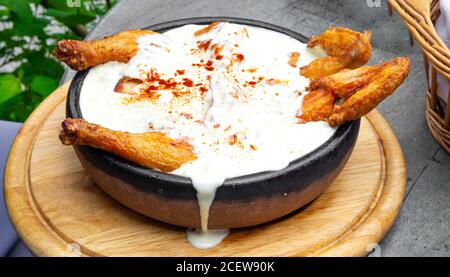 Hot Fried Chicken tobacco with golden brown crust in frying pan on wooden background with herbs and spicy white sauce Stock Photo