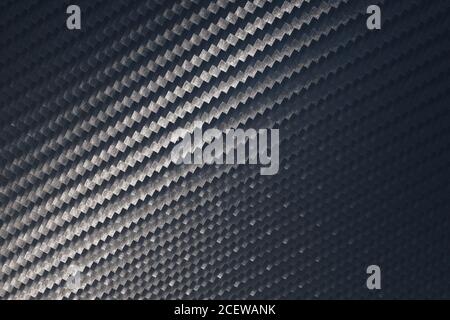 Surface texture of an industrial woven carbon fibre or graphite sheet with a beam of light playing across from the bottom corner highlighting the stru Stock Photo