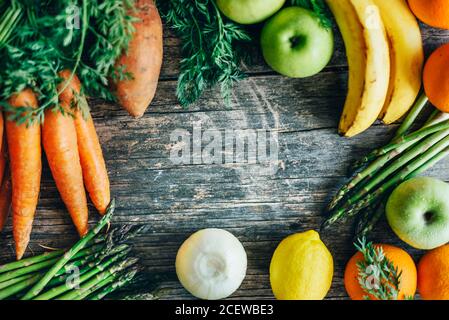 Healthy bio food ingredients frame background from above. Top view of organic superfood border on rustic wooden table. Colorful fruits and vegetables Stock Photo