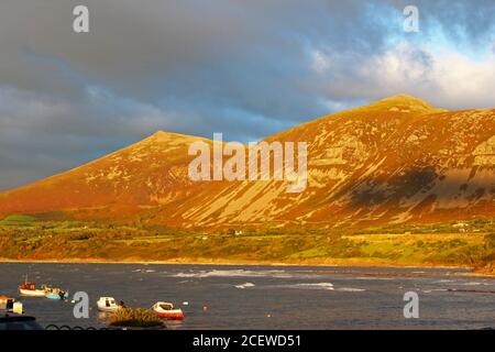 Beautiful sunset lighting on mountains (Yr Eifl) with sea in front of them and dark clouds at Trefor, North Wales Stock Photo