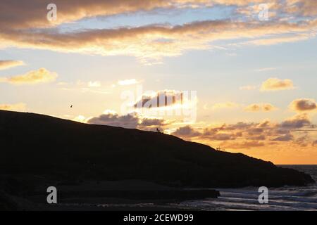 Beautiful orange golden glowing sunset over a headland and sea bay with silhouettes of people at Trefor, North Wales Stock Photo