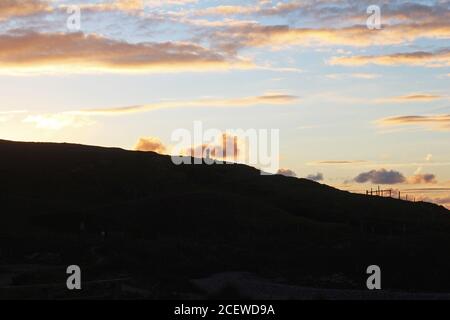 Beautiful orange golden glowing sunset over a headland and sea bay with silhouettes of people at Trefor, North Wales Stock Photo