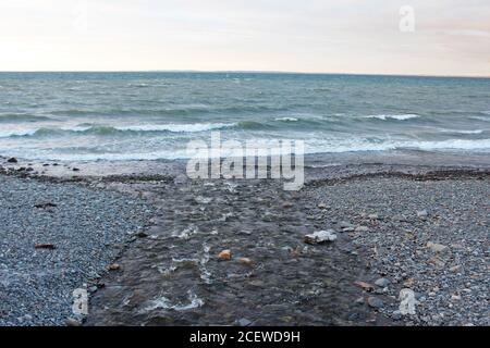 Point where a stream meets the choppy sea on a rocky beach at Trefor, North Wales Stock Photo