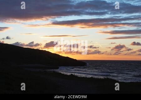 Beautiful orange and pink sunset with pretty clouds over a headland and sea bay at Trefor, North Wales Stock Photo