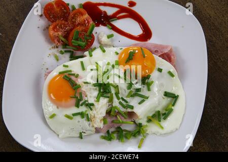 Top view on fried eggs on brad with jam, tomatoes and green fresh chives Stock Photo