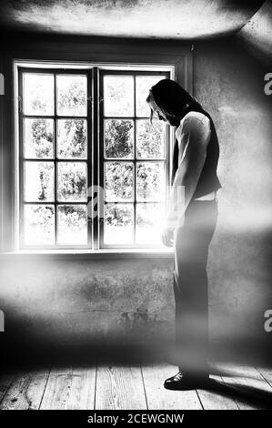 Creative black and white textured image of sad man in front of a window. Stock Photo