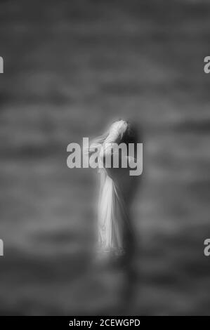 Surreal blurred black and white image of unrecognizable woman standing in water.