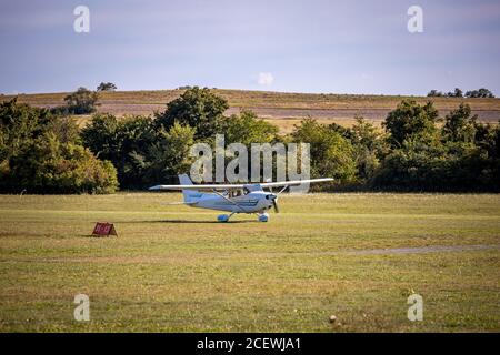 Small white airplane landing on a grass field during a sunny day Stock Photo