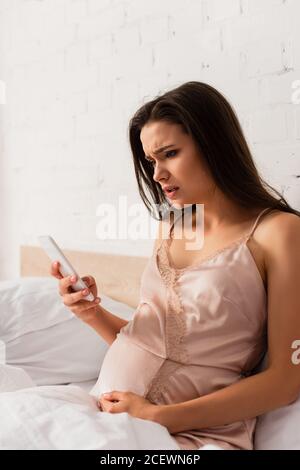 worried and pregnant woman using smartphone in bedroom Stock Photo