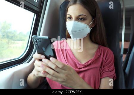 Relaxed woman with KN95 FFP2 face mask using smart phone app. Train passenger with protective mask traveling sitting in business class texting on mobi Stock Photo