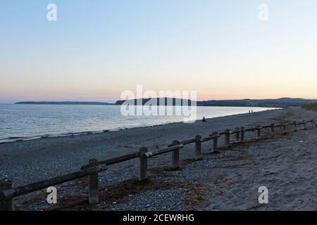 Beautiful Irish Sea shore bay and pebble beach at sunset with wooden fence on Pwllheli beach, North Wales Stock Photo
