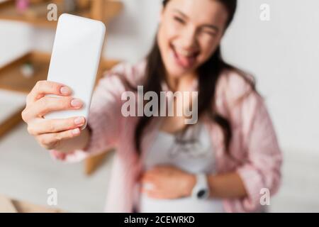 selective focus of pregnant woman sticking out tongue while taking selfie Stock Photo