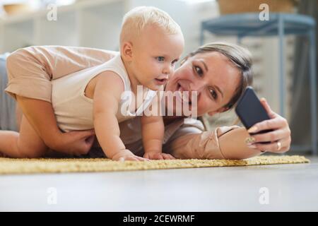 Horizontal level portrait shot of happy young mother taking selfie with her baby son, copy space Stock Photo