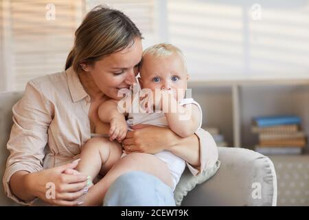 Horizontal medium portrait of attractive Caucasian woman wearing casual outfit sitting with her baby on lap, copy space Stock Photo