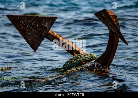 Rope-wrapped rusty anchor in the sea Stock Photo