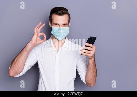 Portrait of his he attractive healthy guy wearing safety mask using device app 5g showing ok-sign stop influenza pandemia healthcare stay home order Stock Photo