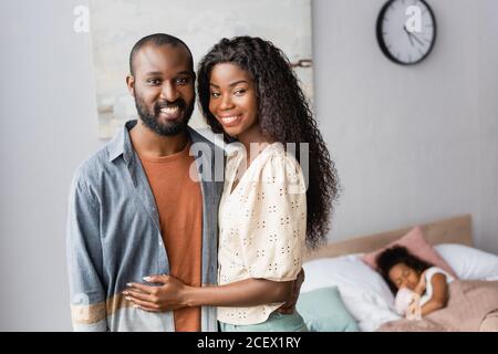 young african american couple looking at camera while standing near daughter sleeping in bed Stock Photo
