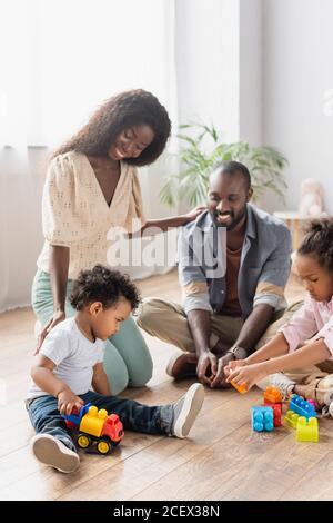 young african american parents in casual clothes near children playing on floor with building blocks Stock Photo