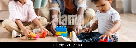 cropped view of african american father with children playing with building blocks on floor, panoramic shot Stock Photo