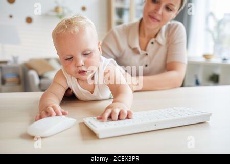 Lovely little baby playing with computer keyboard while his mother holding him, horizontal shot