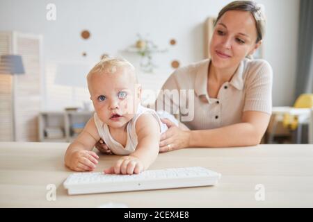 Funny little baby trying to play with computer keyboard while his mother holding him, horizontal shot, copy space Stock Photo