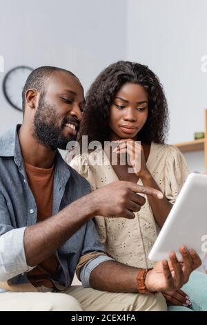 young african american man pointing with finger at digital tablet near pensive wife Stock Photo