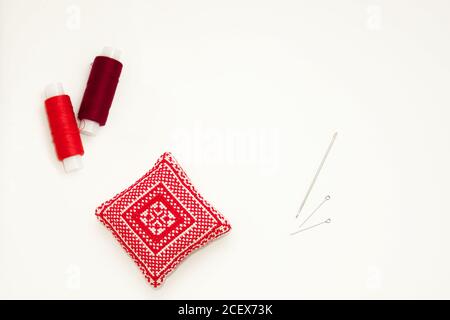 Flat lay with handmade red embroidered needle pad, thread spools, pins, needles, mock up, top view. Layout mockup on blank white background for Stock Photo