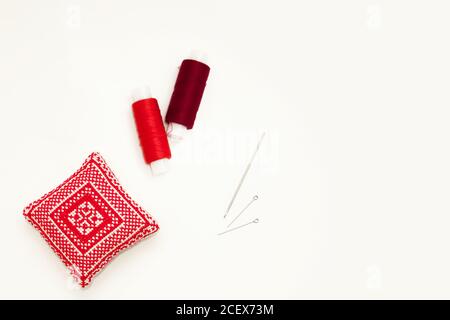 Flat lay with handmade red embroidered needle pad, thread spools, pins, needles, mock up, top view. Layout mockup on blank white background for Stock Photo