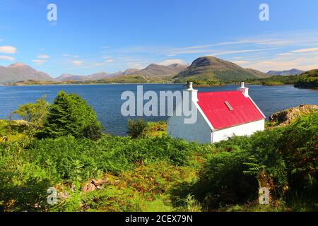 Small Red and White Cottage overlooking Loch Sheildaig with the Torridon Mountains in the distance. West Highlands, Scotland, UK Stock Photo